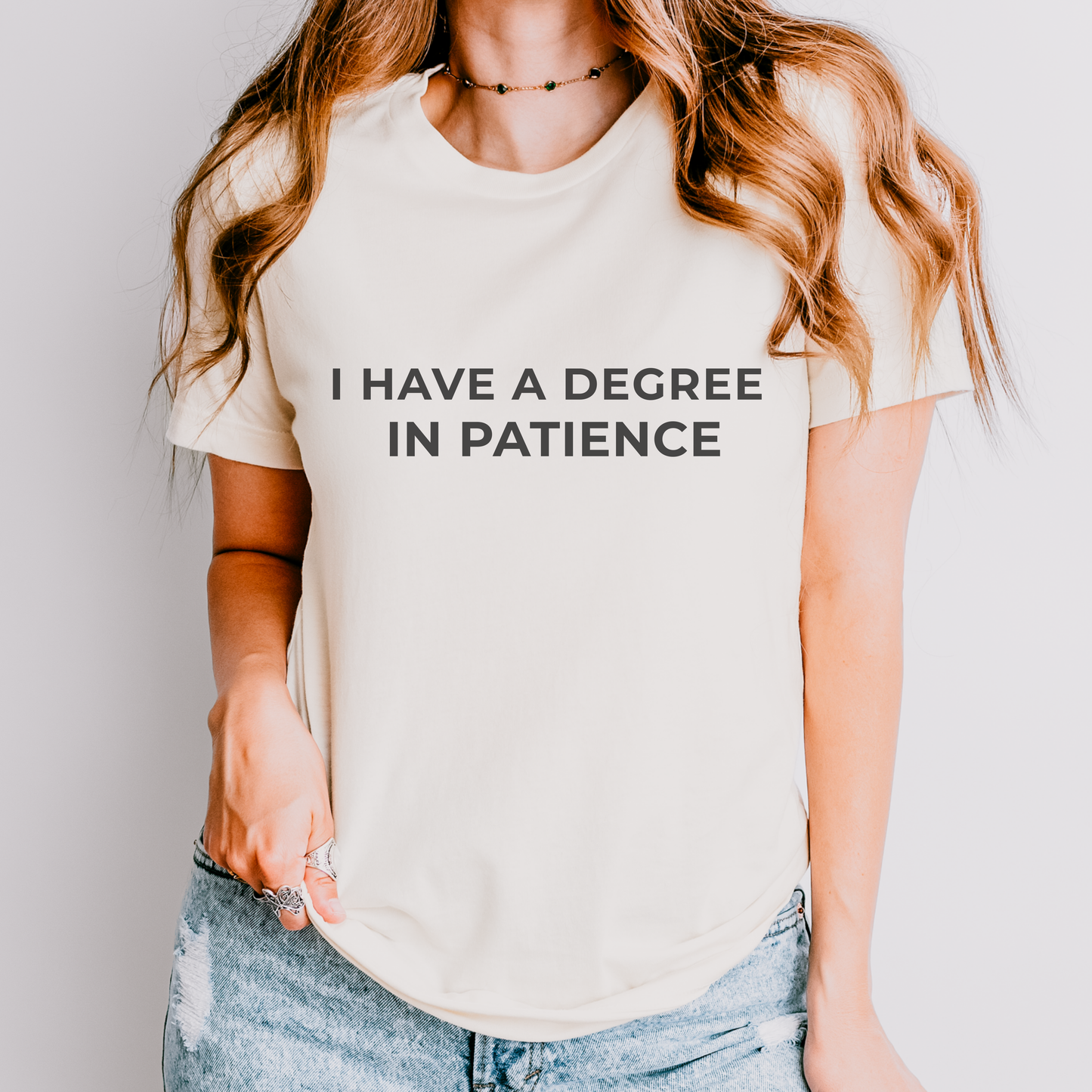 White teacher t-shirt with the phrase “I Have a Degree in Patience” in black text, styled flat with neutral teacher-inspired accessories.