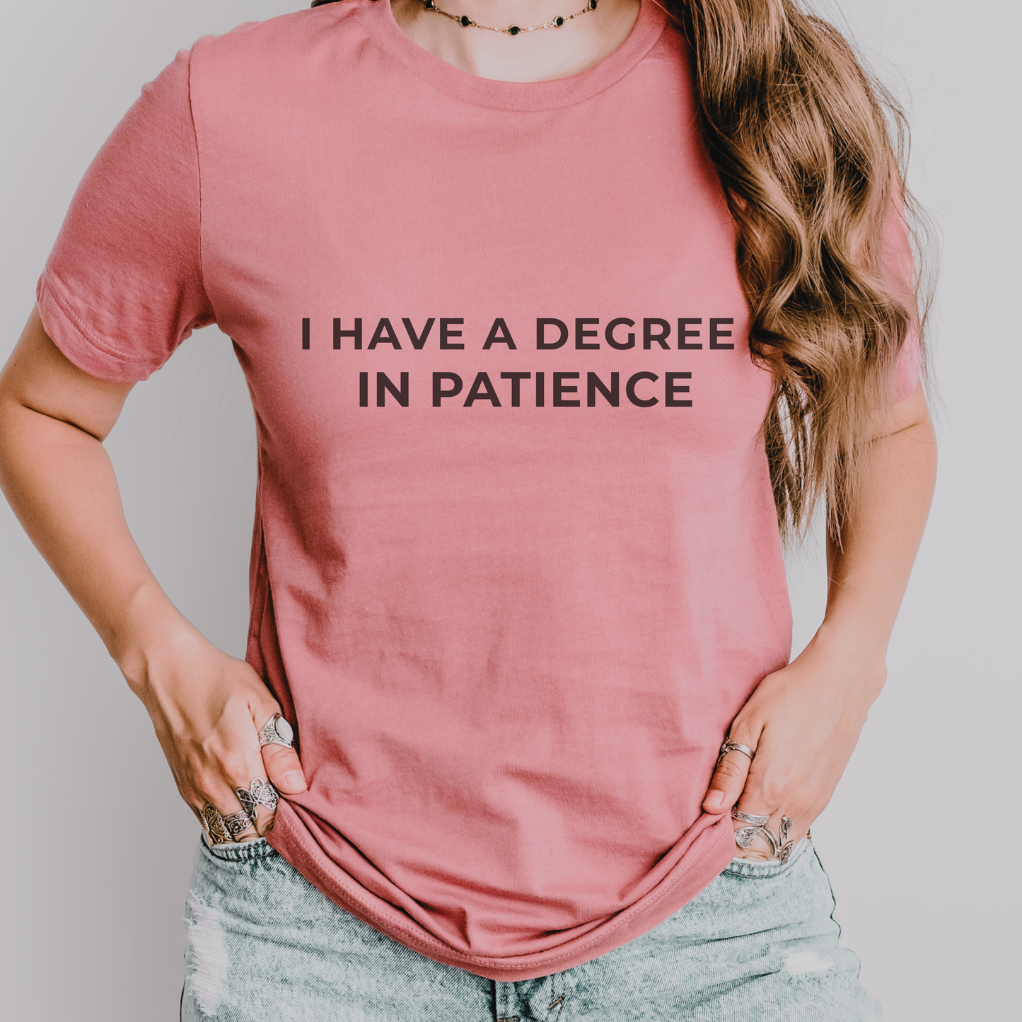 Dusty rose teacher t-shirt with “I Have a Degree in Patience” printed in black, styled with a casual, cozy flat lay look.