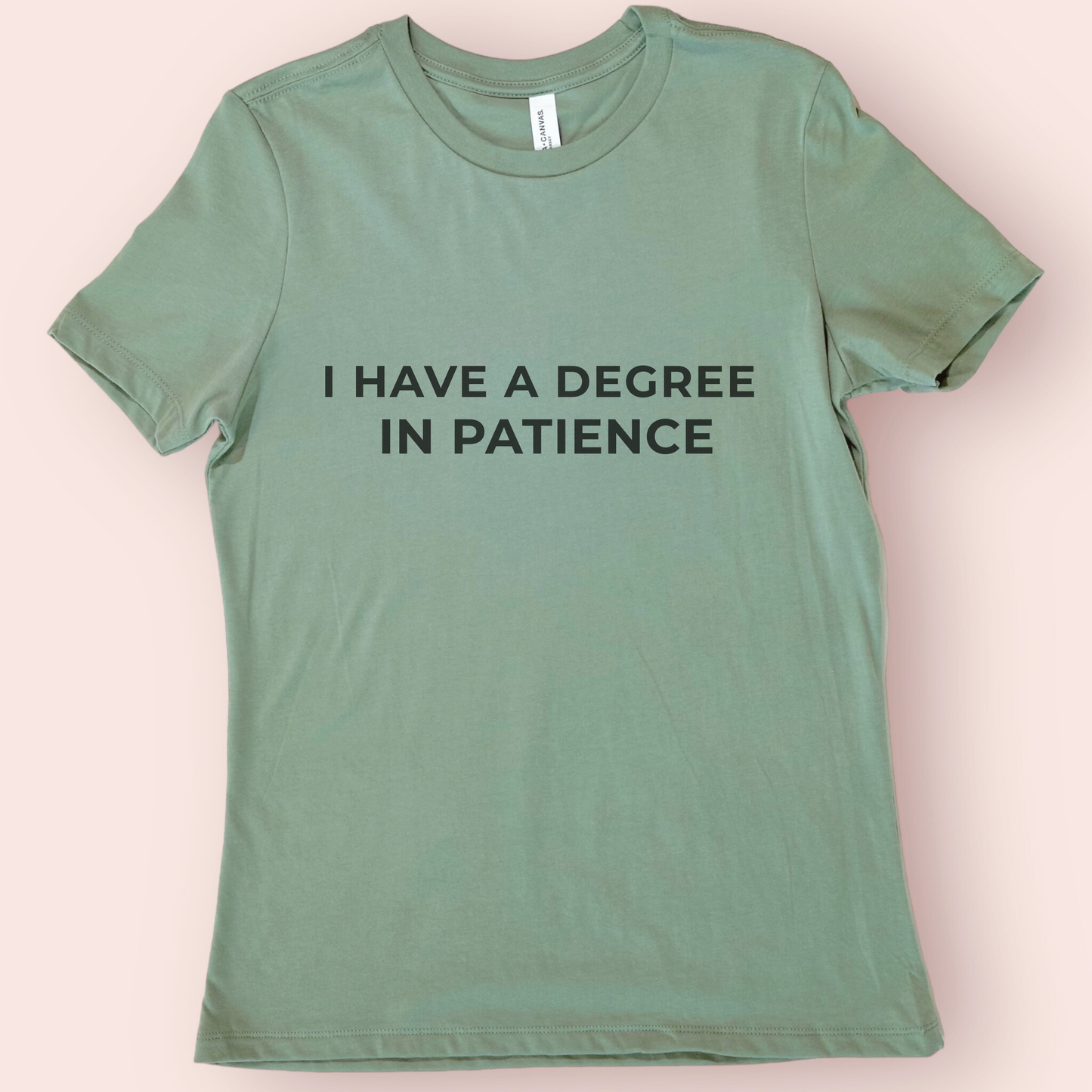 Sage green unisex teacher shirt with black “I Have a Degree in Patience” lettering on a simple background.