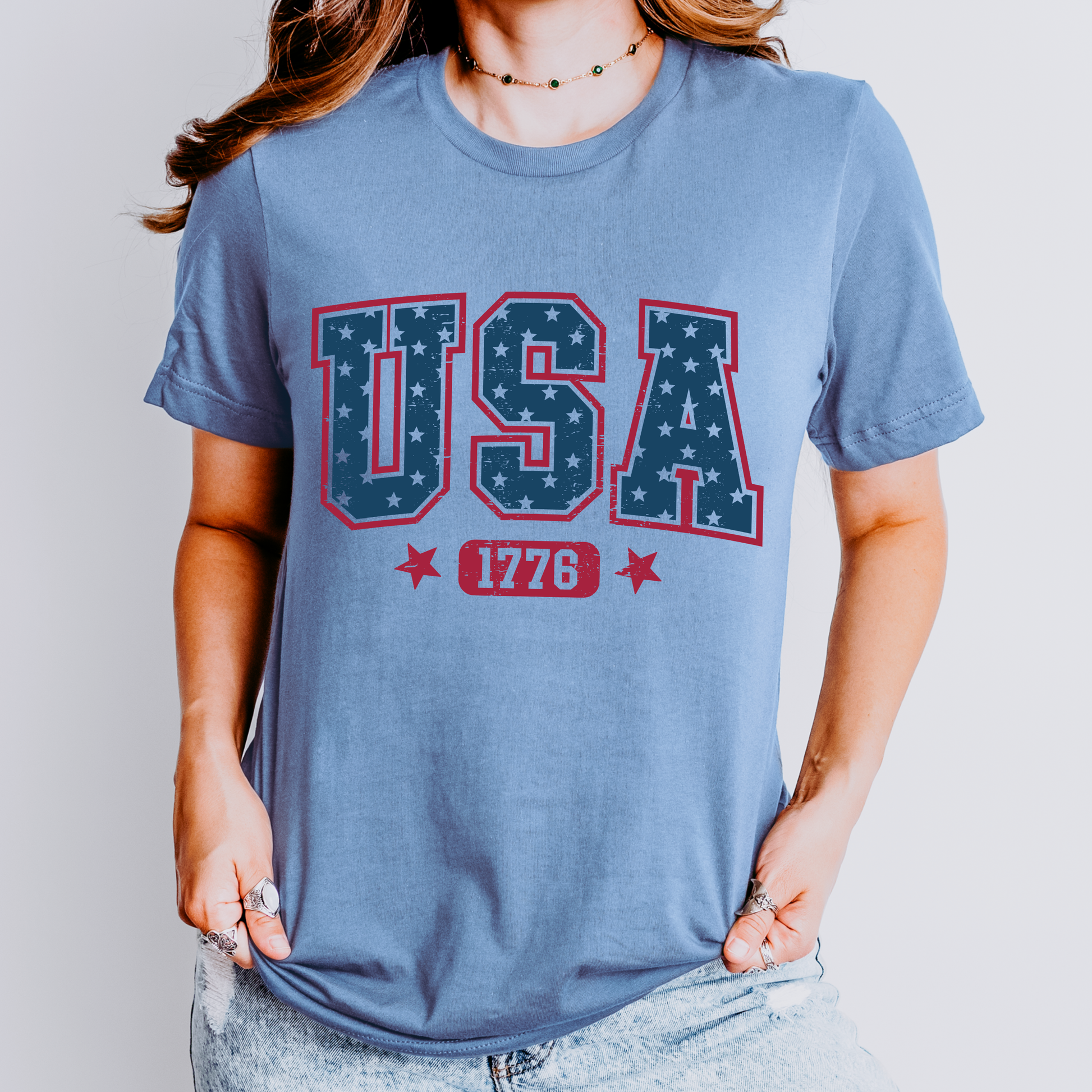 Person wearing a blue t-shirt with 'USA 1776' design on a plain background