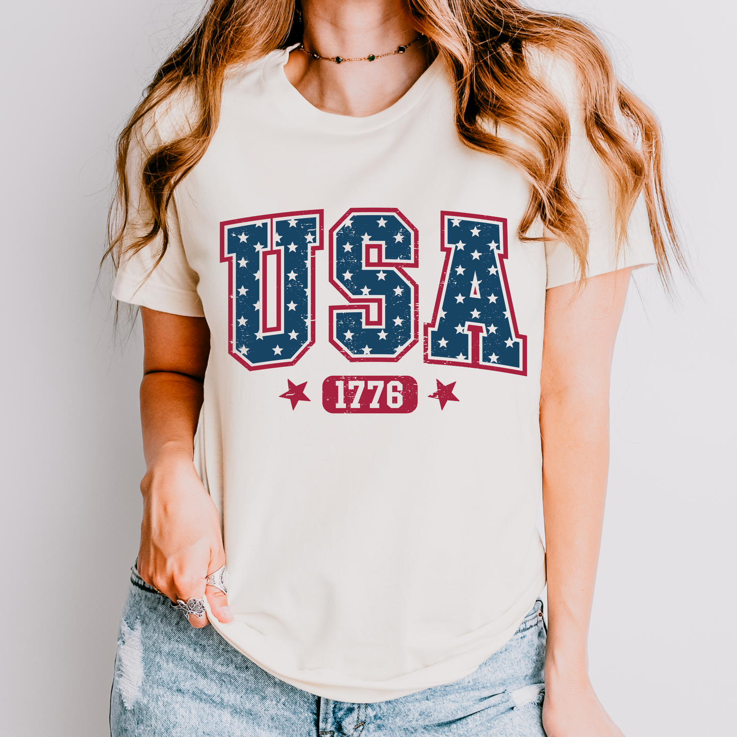 Person wearing a white t-shirt with 'USA 1776' design on a plain background