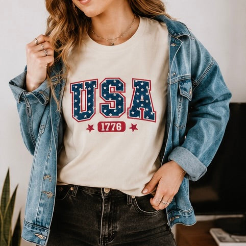 Person wearing a white t-shirt with 'USA 1776' design, denim jacket, and black pants.